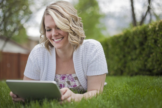 A young woman reading using a handheld electronic device, or e reader.
