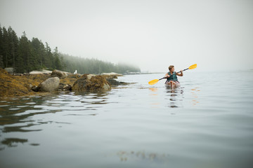 A man paddling a kayak on calm water in misty conditions. New York State, USA