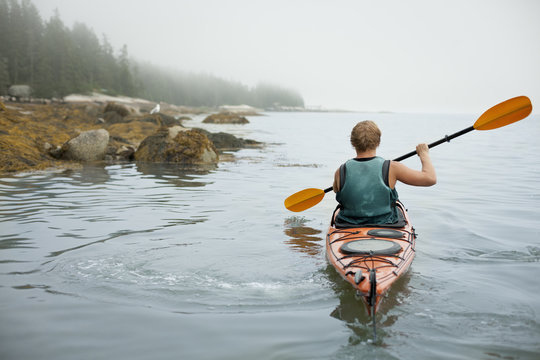 A man paddling a kayak on calm water in misty conditions. New York State, USA
