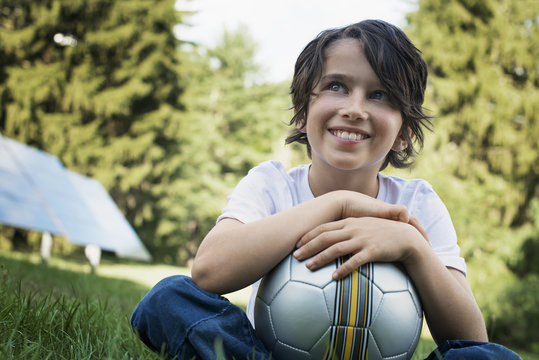 A boy holding a football, sitting on the grass. Solar panels. 