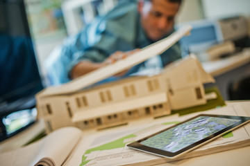 Architects working on a green construction project, using computer technology, in an office. An architect's model of a house. Computer tablet. 