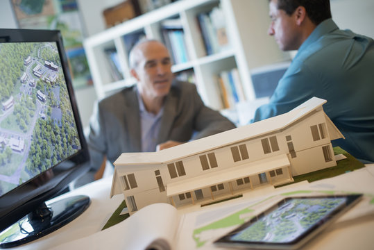 Architects working on a green construction project, using computer technology, in an office. Scale model of a building.