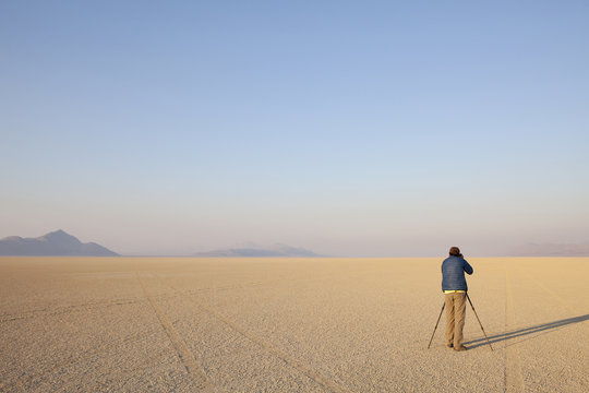 Man with camera and tripod on the flat saltpan or playa of Black Rock desert, Nevada.