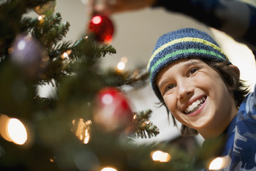 A young boy holding Christmas ornaments and placing them on the Christmas tree. 