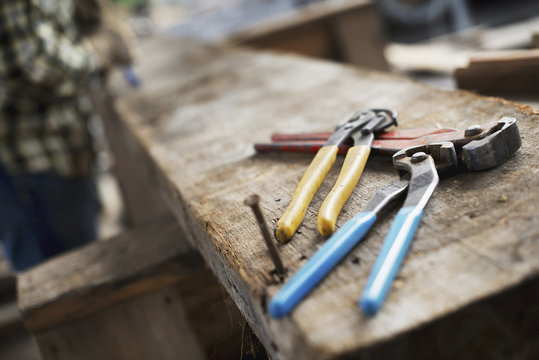 A reclaimed lumber workshop. A person at a workbench, and tools, grippers and pliers lined up on a plank of wood.