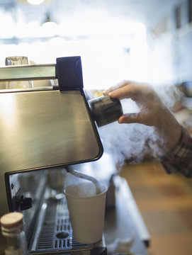 A person, barista making coffee, and frothing milk using a steam pipe. Coffee shop.
