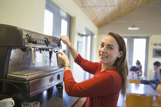 A young woman making coffee using a large coffee machine.