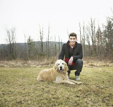 A man in the open air, on a winter day.  Stroking a golden retriever dog.