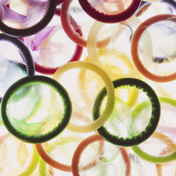 A large group of multi-colored condoms displayed on a white background. Heaped up.