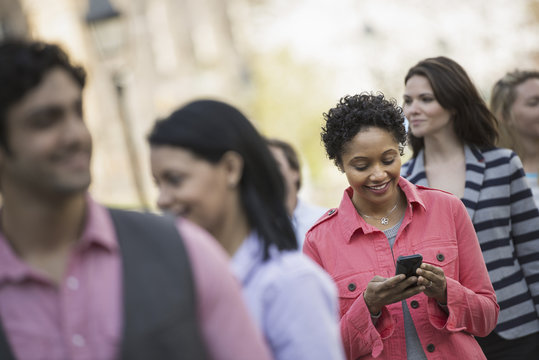 People outdoors in the city in spring time. A woman standing among a group checking her cell phone.