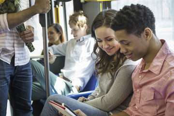 Urban Lifestyle. A group of people, men and women on a city bus, in New York city. A couple side by side looking at a digital tablet.
