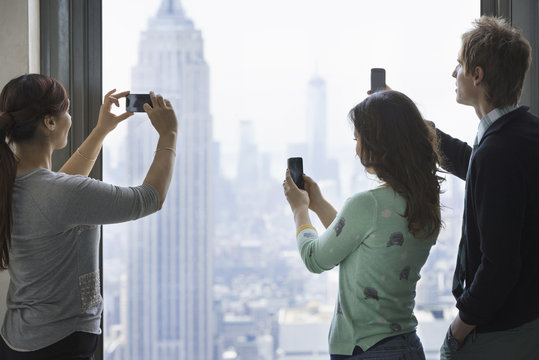 Urban lifestyle. Three people standing on an observation deck, using their phones to take images of the view over the city.