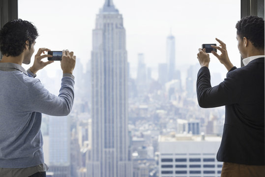 Urban lifestyle. Two young men using their phones to take images of the city from an observation platform overlooking the Empire State Building.