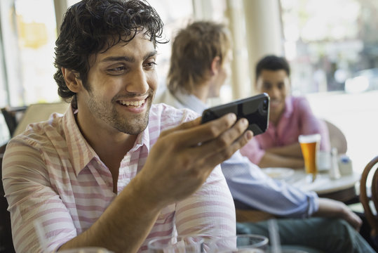 Urban Lifestyle. Three young men around a table in a cafe. One using his smart phone