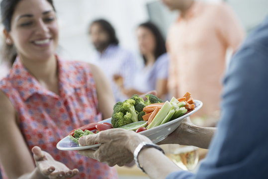 An open plan office in New York City. A working lunch, a salad buffet. A group of men and women of mixed ages and ethnicities meeting together.