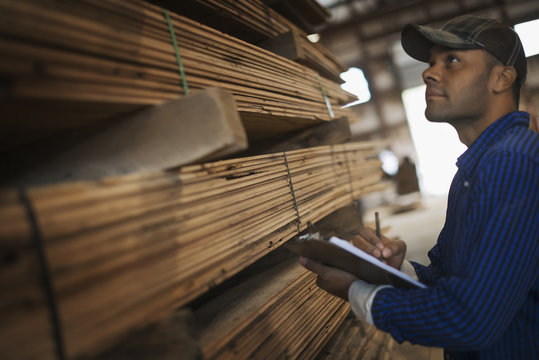 A heap of recycled reclaimed timber planks of wood. Environmentally responsible reclamation in a timber yard. A man with a clipboard by a rack of planks. 