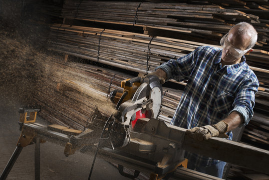 A reclaimed lumber workshop. A man in protective eye goggles using a circular saw to cut timber. 