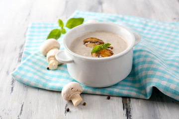 Mushroom soup in white pot, on napkin,  on wooden background