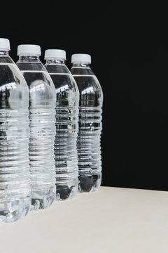 Row of clear, plastic water bottles filled with filtered water in a row. on a black background. 