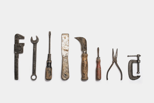 Used tools arranged in a row. Well used, worn handles, shaped wooden smooth texture. Metal rusty and marked implements. 
