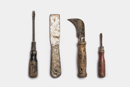 Used tools arranged in a row. Well used, worn handles, shaped wooden smooth texture. Metal rusty and marked implements. 