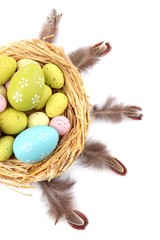 Easter eggs in nest and decorative feathers, isolated on white