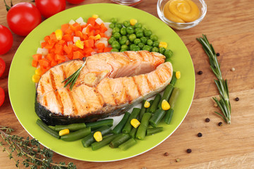 Tasty grilled salmon with vegetables, on wooden table