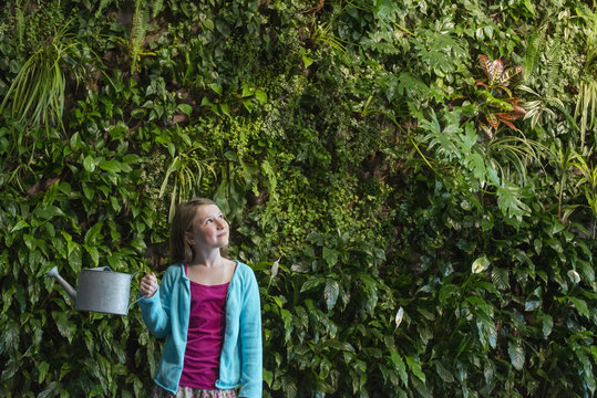 A young girl standing in front of a wall covered with ferns and climbing plants. 