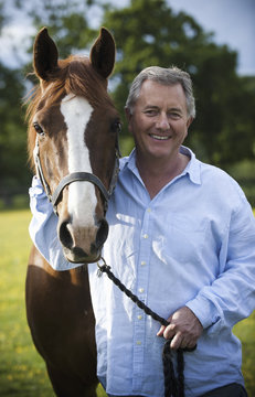 A man standing holding the halter of a bay horse with a white flash on its muzzle. 