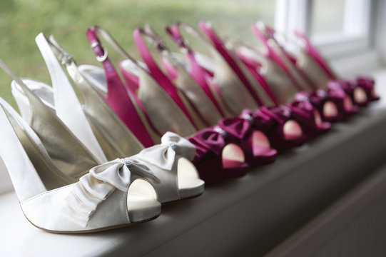 A row of high heeled shoes. Pairs of peep toe slingbacks in white and pink.  Special occasion. 