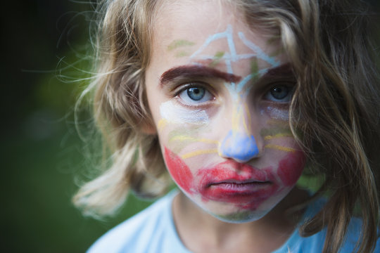 A young girl with a face decorated with face paints, wearing an unamused expression.