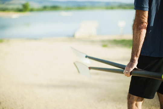 A middle-aged man carrying oars and walking down a pontoon towards the river.