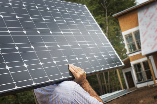 A workman carrying a large solar panel at a green house construction site.