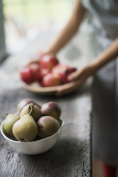A person preparing organic fresh produce in a kitchen. Tray of red apples.  Bowl of pears.