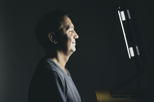 Smiling middle aged man sitting in front of a light therapy box, a full spectrum light box which mimics the sun, and treats people suffering from seasonal affective disorder.
