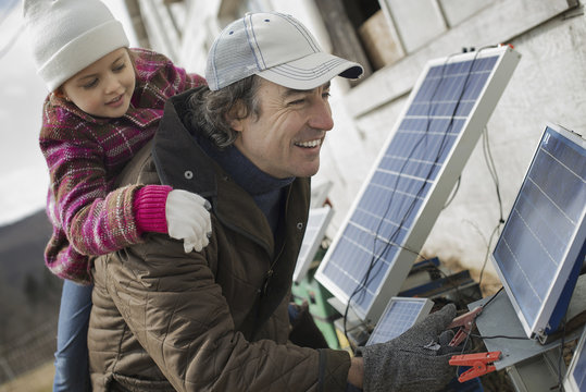 A man giving a child a piggybank while trying to connect the leads for solar power panels.
