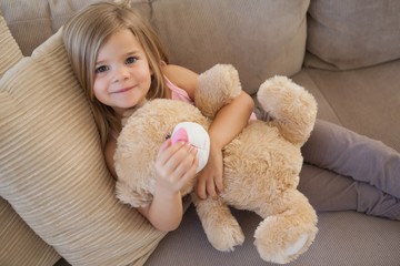 Portrait of a smiling girl with stuffed toy sitting on sofa