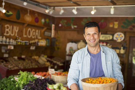 A farm growing and selling organic vegetables and fruit. A man holding a bowl of basket of freshly picked tomatoes.