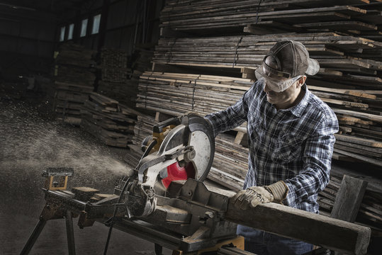 A reclaimed lumber workshop. A man in protective eye goggles using a circular saw to cut timber.