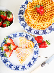Crisp golden fresh baked waffle topped with strawberries on whit