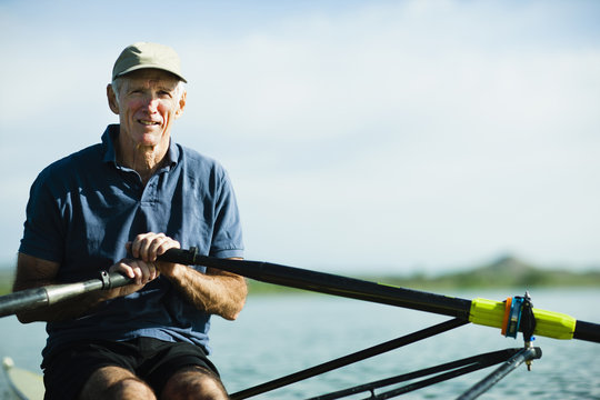 A middle-aged man rowing a single scull rowing boat on the water. 