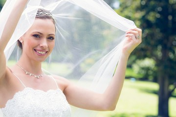 Happy young bride unveiling self in garden