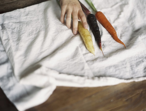 A domestic kitchen table. A person arranging fresh carrots on a white cloth.