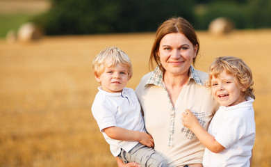 Young mother and two little twins boys having fun on yellow hay