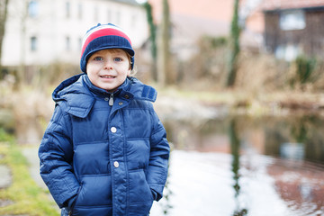 Portrait of cute caucasian toddler boy in warm clothes on cold d