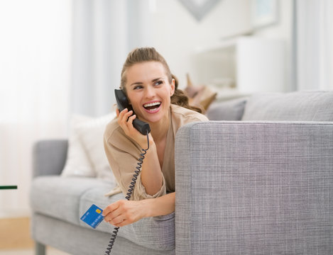 Happy woman with credit card laying on sofa and talking phone