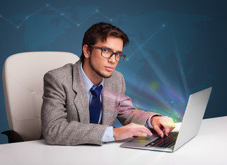 Handsome man sitting at desk and typing on laptop with abstract