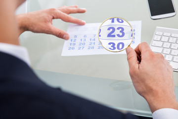 Businessman Looking At Calendar Through Magnifying Glass