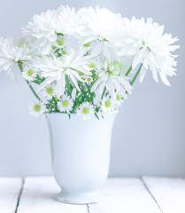 Daisies in white vase on wooden background