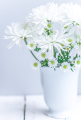 Daisies in white vase on wooden background
